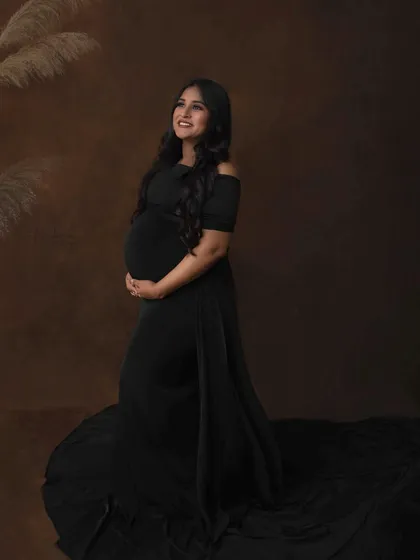 A hopeful and radiant portrait, with the mother-to-be looking up with a bright smile. The flowing black gown and simple styling create a look that is both elegant and timeless.