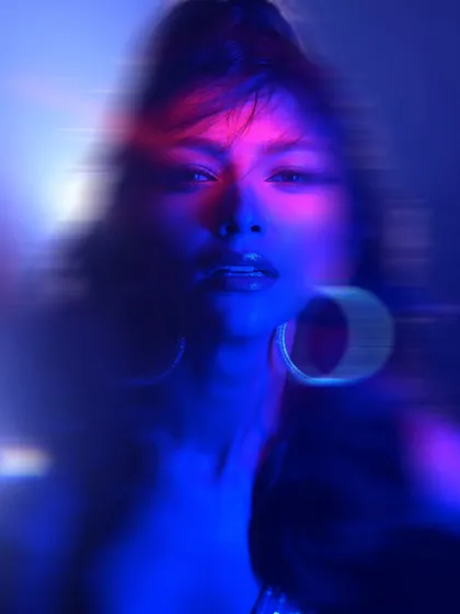 An experimental close-up with dramatic blue and pink lighting. The light trails from the hoop earrings add to the abstract and energetic feel of this portrait.