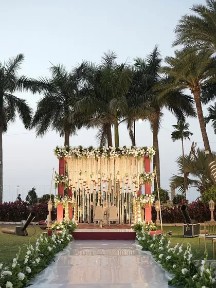 This outdoor mandap combines traditional elegance with a tropical setting. The stage is framed by lush palm trees, with a beautiful floral canopy of white tuberose and red accents creating a classic and vibrant look.