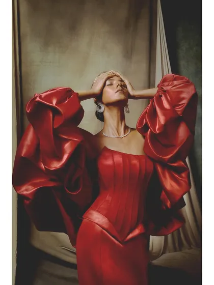 An emotive pose from the Ambika Lal campaign. The vibrant red satin of the corseted gown and voluminous sleeves fills the frame, creating a powerful statement of passion and drama.