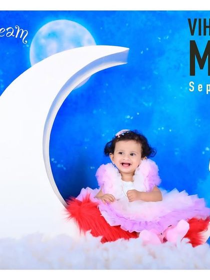 A dreamy "baby on the moon" theme, with a little girl in a beautiful dress sitting on a crescent moon prop.