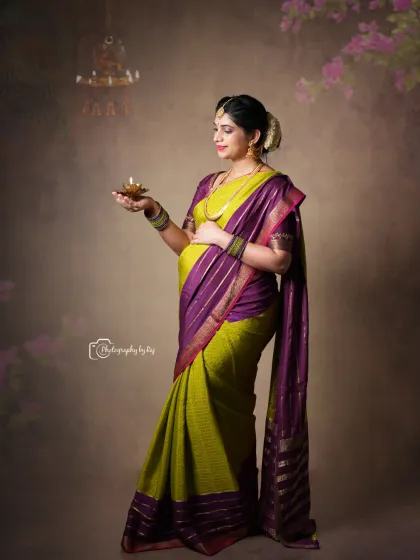A divine studio portrait of a mother-to-be in a traditional saree, holding a diya (oil lamp). The lighting creates a warm and spiritual glow.