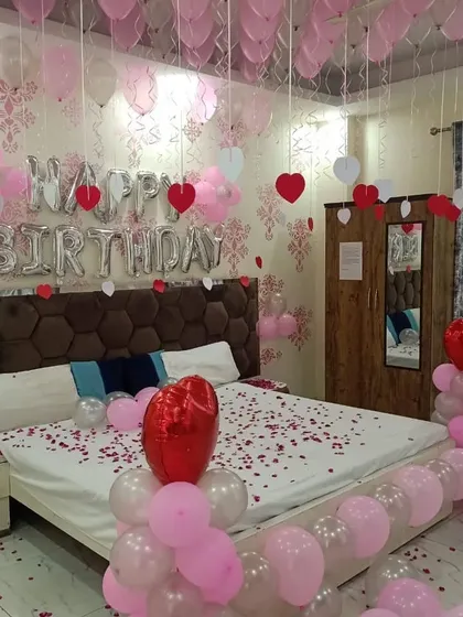 A sweet pink and white birthday room surprise with ceiling balloons, foil letters, and rose petals scattered on the bed.