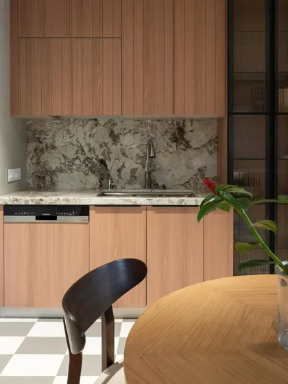 This view shows the seamless integration of the dishwasher and sink area within the wood-toned cabinetry. The design prioritizes a clean, uncluttered look, allowing the beauty of the materials like the marble backsplash to stand out.