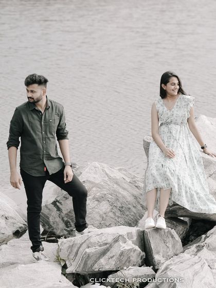 A couple poses on rocks by a lake, their casual outfits and the natural setting creating a relaxed and scenic pre-wedding photo.