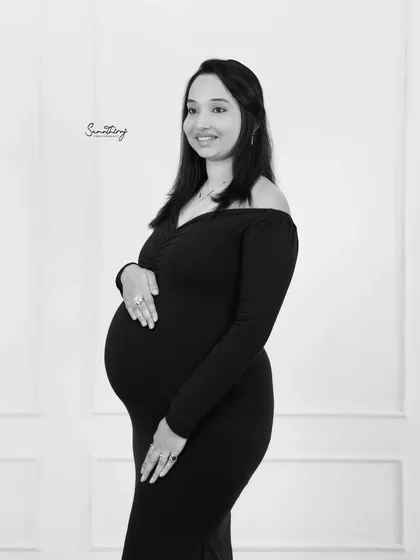 A simple and beautiful black and white portrait of a mother-to-be in a classic black dress. The clean background and soft lighting highlight her natural glow and elegant silhouette.