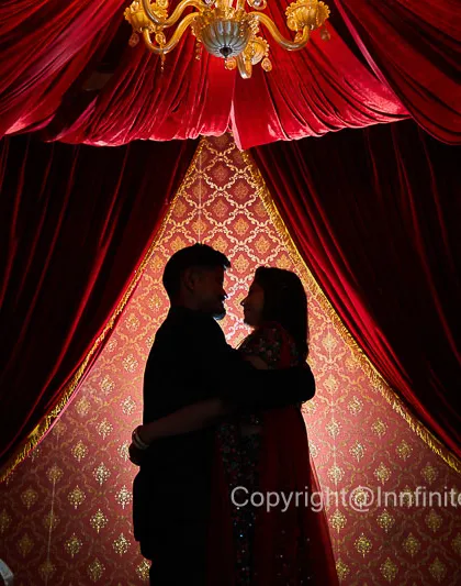 A silhouette captured against a rich, theatrical red curtain backdrop. This technique creates a sense of intimacy and drama, focusing entirely on the couple's embrace.