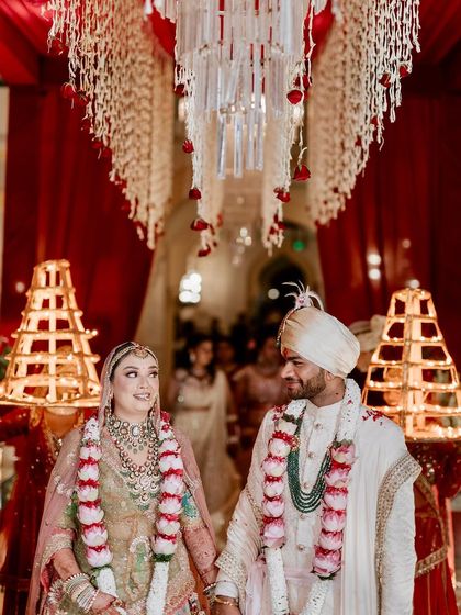 The couple during their wedding ceremony in Jaipur, with a backdrop of traditional temple bells and hanging floral arrangements.