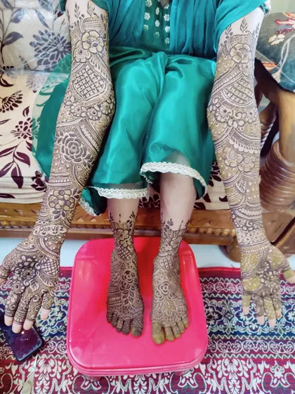 This bride is showcasing her complete mehndi, with full coverage on her arms and feet, ready for her wedding day.