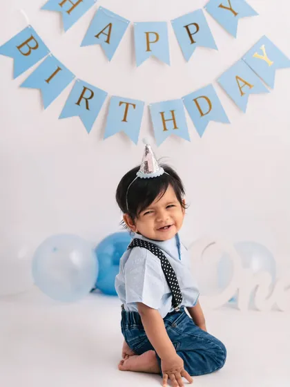 A cheeky little smile from the birthday boy. Dressed in a party hat and cute suspenders, he's ready for his first birthday celebration.