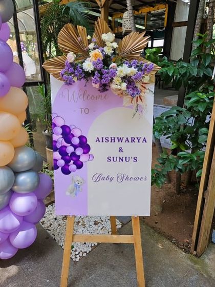 A personalized welcome sign for Aishwarya & Sunu's baby shower, topped with a lavish floral arrangement.