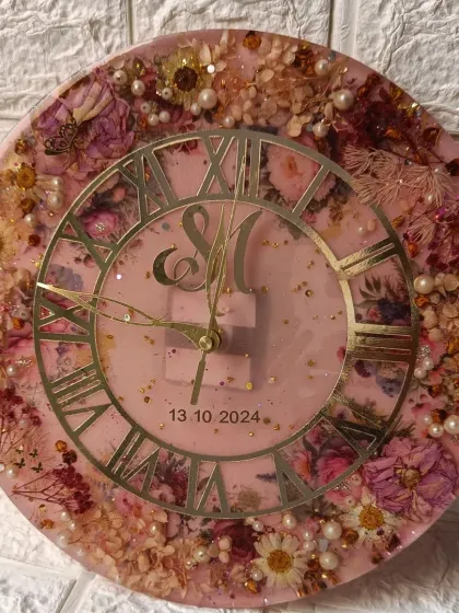 A beautiful 12-inch floral wall clock with a soft pink background. The preserved flowers are a mix of the client's varmala and other complementary blooms, creating a full and lush design.