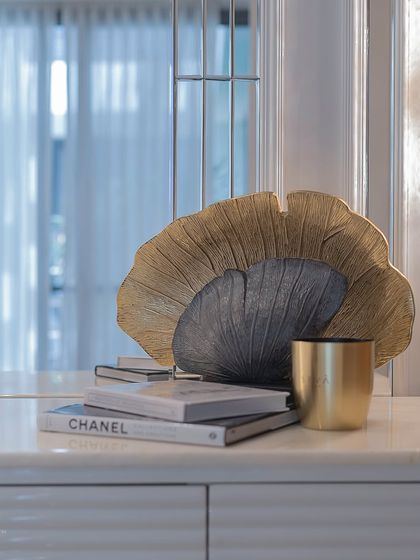 This credenza stands pretty, hides the chaos, and demands a second look. The decor piece, a sculptural fan-like object in gold and grey, adds depth and artistry to the styled surface.