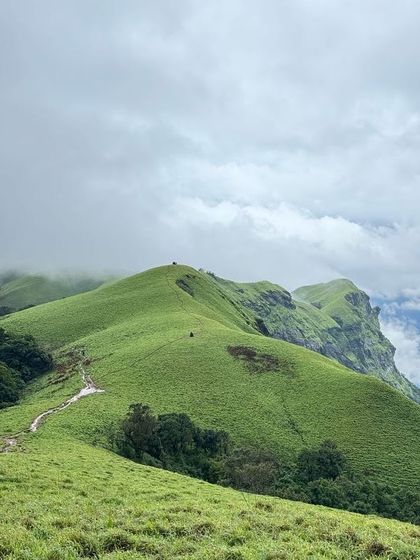 The vast, rolling green meadows of the Bandaje trek, with the trail winding its way towards the peak.