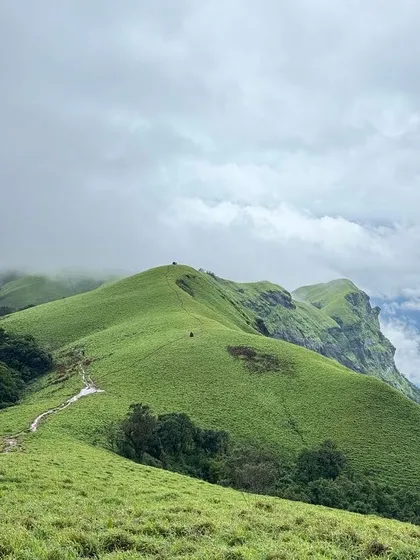 The vast, rolling green meadows of the Bandaje trek, with the trail winding its way towards the peak.