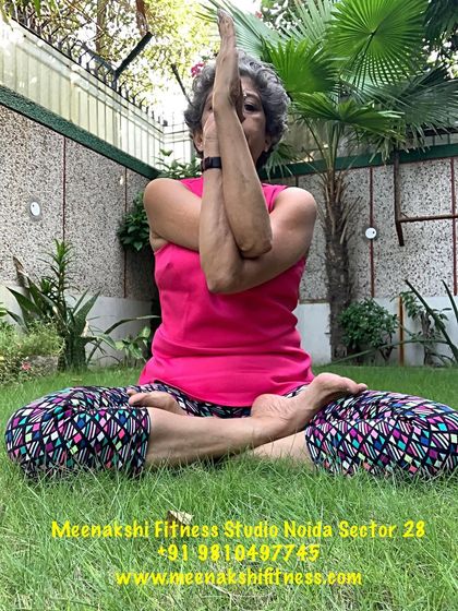 The seated Gomukhasan, or Cow Face Pose, in a peaceful garden setting. This posture stacks the knees and opens the hips deeply.