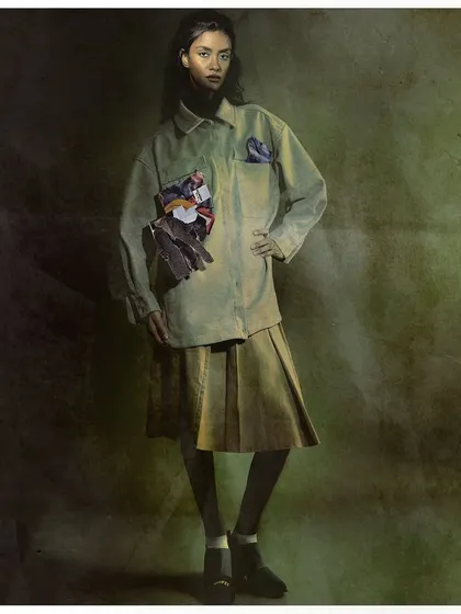 A full-length shot from 'from the pages,' showing how the conceptual collage element is integrated into a complete outfit. The painterly background adds to the artistic, editorial feel.
