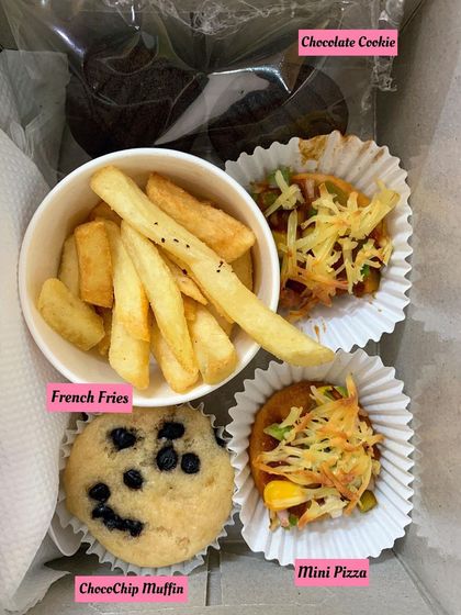 A close-up of a party box with french fries, a choco-chip muffin, mini pizzas, and a chocolate cookie. It's a perfect balance of sweet and savory for kids.