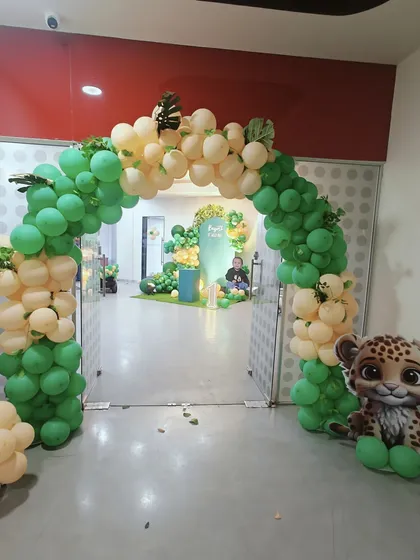 A welcoming arch for a jungle-themed first birthday. The organic arrangement of green and cream balloons, accented with tropical leaves, creates a perfect entrance to a wild and fun celebration.
