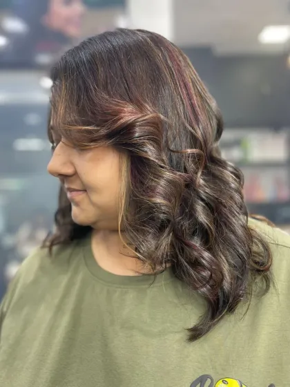 A shoulder-length cut with soft curls and subtle red highlights, adding a touch of warmth and dimension to the hair.