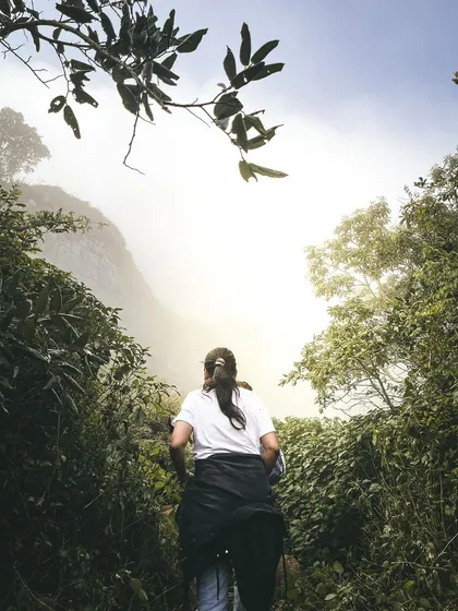 The final push to the summit. A trekker makes her way through the dense, misty forest path just before reaching the top of Skandagiri.