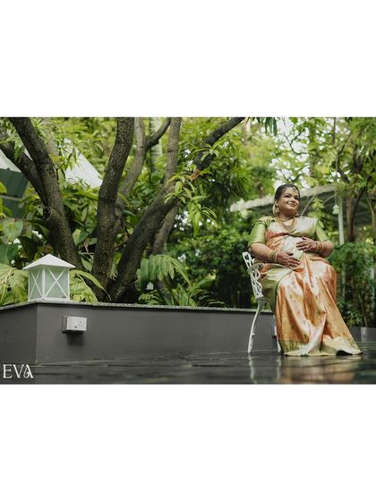 A serene portrait of a mother-to-be seated in a garden, gently holding her belly and smiling. The natural light and verdant background create a peaceful and organic feel.