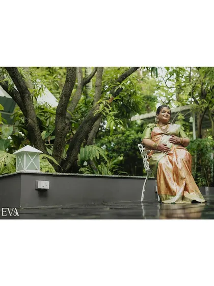 A serene portrait of a mother-to-be seated in a garden, gently holding her belly and smiling. The natural light and verdant background create a peaceful and organic feel.