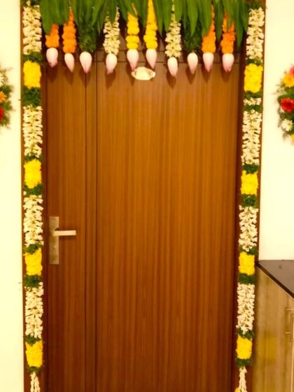 A simple and elegant housewarming flower decoration for an apartment door. The door frame is decorated with flower garlands and two small bouquets.