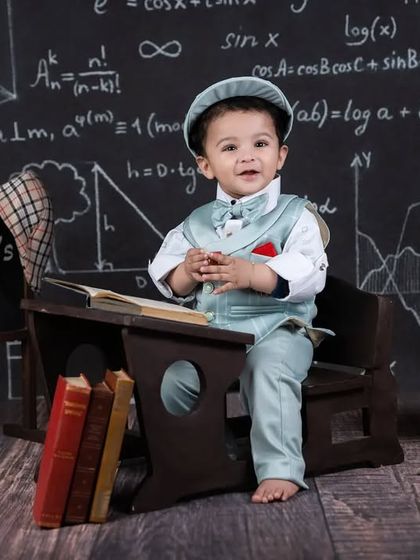 This little gentleman is ready for class, dressed in a suit and sitting at his desk with a happy expression.