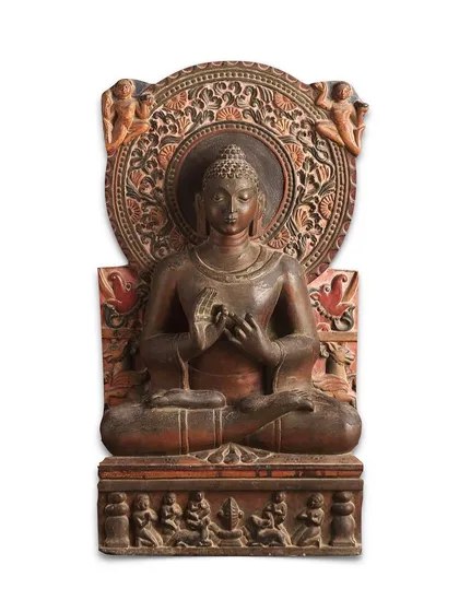 This magnificent stone stele of Gautam Buddha from 8th century North India is a testament to the rich history of ancient Indian sculpture. The Buddha is depicted seated in 'dhyanasana' with his hands in the 'dharmachakra' mudra, conveying a serene expression. The intricate details, from the scrolling nimbus to the worshippers on the throne, highlight its historical and artistic importance.