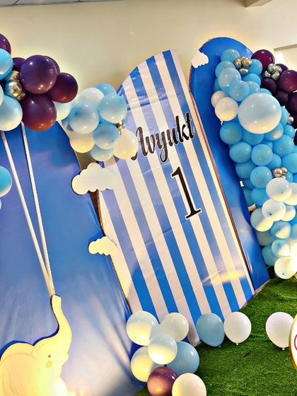 A sweet baby elephant theme for a first birthday. The decor is set in a lovely blue and white palette, with elephant cutouts, cloud details, and a striped backdrop, creating a dreamy and gentle atmosphere.