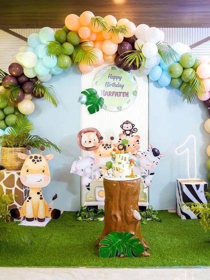 A stunning jungle safari themed backdrop for a first birthday, featuring cute cartoon animals, a tree stump cake stand, and a lush balloon arch.
