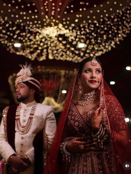 A stunning portrait of the bride and groom under a canopy of lights. Her makeup is flawless, with a focus on creating a radiant complexion that glows from within.