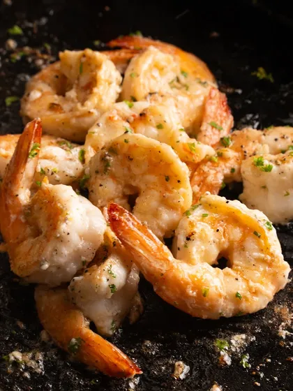 A close-up of butter garlic prawns, fresh from the kitchen. The dark, textured surface makes the prawns pop.