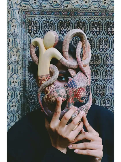 A striking image from 'Roots' where the model's face is partially obscured by an ornate, hand-painted mask. This styling choice explores the idea of identity as both a shield and a form of expression.