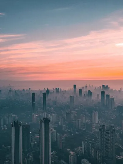 A drone's perspective of Mumbai's skyline, edited with a cool, teal-and-orange tone to create a post-apocalyptic mood at sunset.
