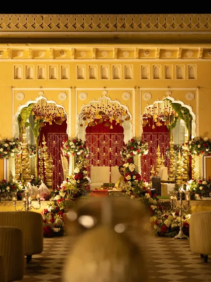 The wedding mandap setup, rich in traditional elements with red and gold decor, set against the warm yellow walls of the palace courtyard.