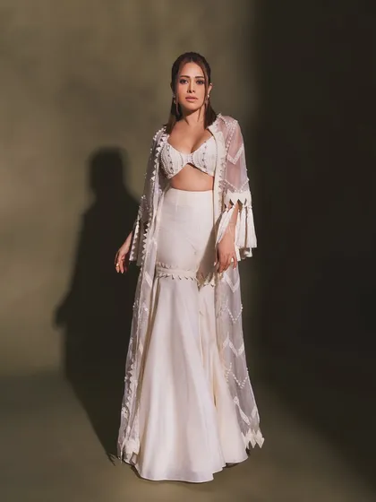 Pearls and tassels make this white indo-western outfit on Nushrratt Bharuccha truly special. The fringed jacket adds a playful, bohemian touch to the elegant sharara set.