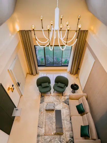 This high-angle view of a Guwahati residence captures the full scope of a cohesive lighting plan. The modern chandelier draws the eye, while subtle wall and accent lights create a warm, layered glow throughout the double-height living space.