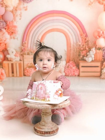 A sweet portrait from a first birthday session, with cake on her cheek and a curious look. The warm, pastel tones of the setup complement her adorable expression.