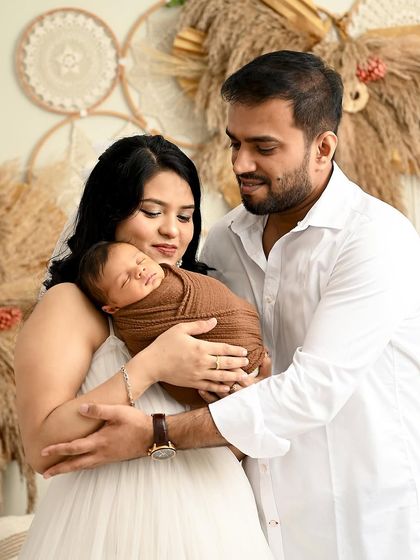 A warm and loving family portrait in our boho studio. The parents embrace their newborn, who is wrapped snugly in a brown swaddle that complements the earthy tones of the set.
