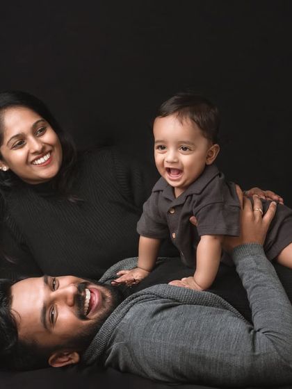 Lying down together creates a casual and intimate family portrait. The baby's joyful expression while playing on dad's chest is a perfect example of the candid, happy moments I love to capture against a simple, dark background.
