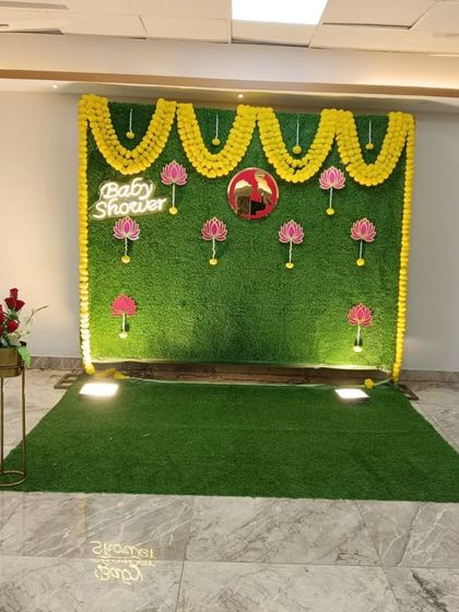 A full view of the traditional baby shower stage with a green backdrop, marigold decor, and lotus accents.