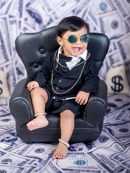 A laugh that's worth a million dollars. This happy "Boss Baby" is enjoying his moment in the spotlight, surrounded by money and looking cool in his shades.