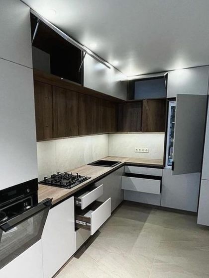 This image displays the kitchen's full functionality with drawers and cabinets open. The combination of white and wood-grain handle-less cabinets, along with a built-in oven, creates a highly ergonomic and modern workspace.