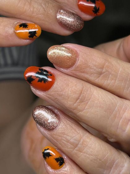 A fun, Halloween-themed manicure. This design features sparkling bronze nails paired with orange accent nails adorned with black bat silhouettes.