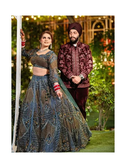 A regal portrait of the couple in their richly detailed outfits, posing in a beautifully lit garden setting at night.