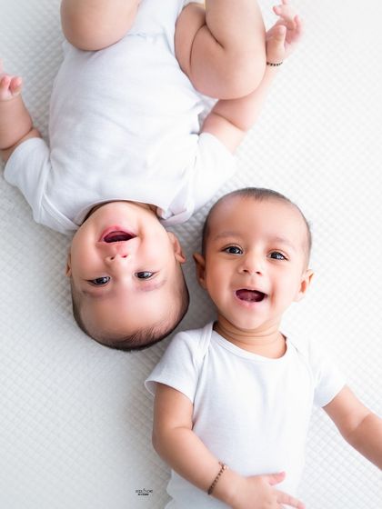 Two happy twin babies lying side-by-side, one upside down, making for a playful and unique portrait.
