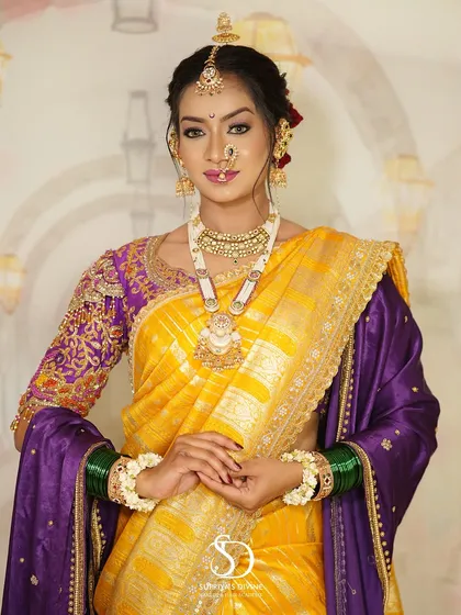 A full-length view of a traditional Marathi bride. The look is complete with a vibrant yellow and purple saree, green glass bangles, and floral bracelets, all tied together with flawless makeup.