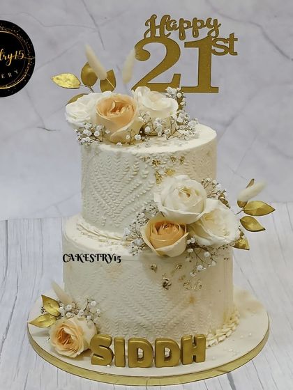A sophisticated two-tier pineapple cake for a 21st birthday. The cake features an elegant engraved pattern and is adorned with beautiful fresh flowers and ferns.
